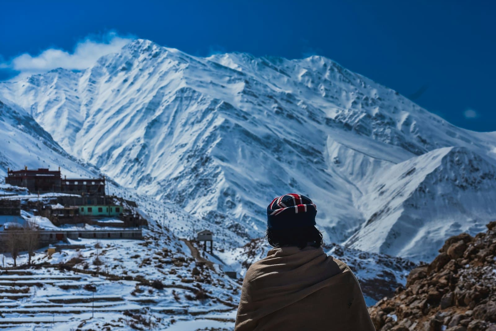 A person wrapped in a shawl looking out at snow-covered Himalayan peaks